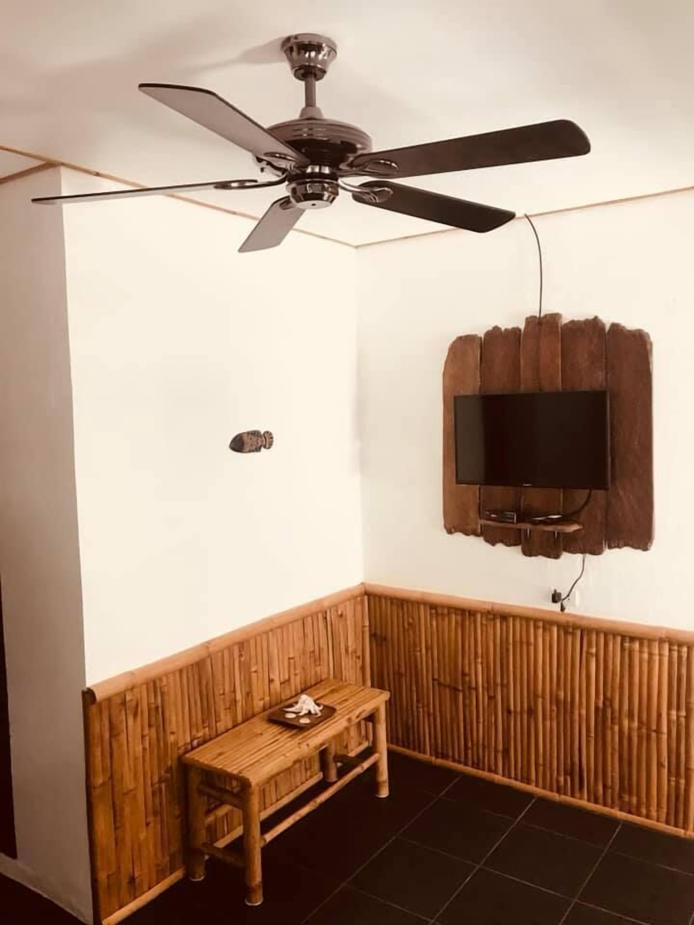 A room with a ceiling fan, a mounted television, a wooden bench, and a bamboo wall panel.