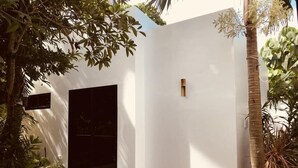 A modern outdoor space with a white wall, a black door, and a small wooden stool.