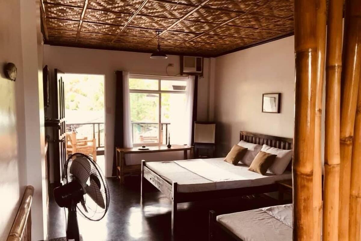 A room with a bed, a desk, a chair, a fan, and a window.
