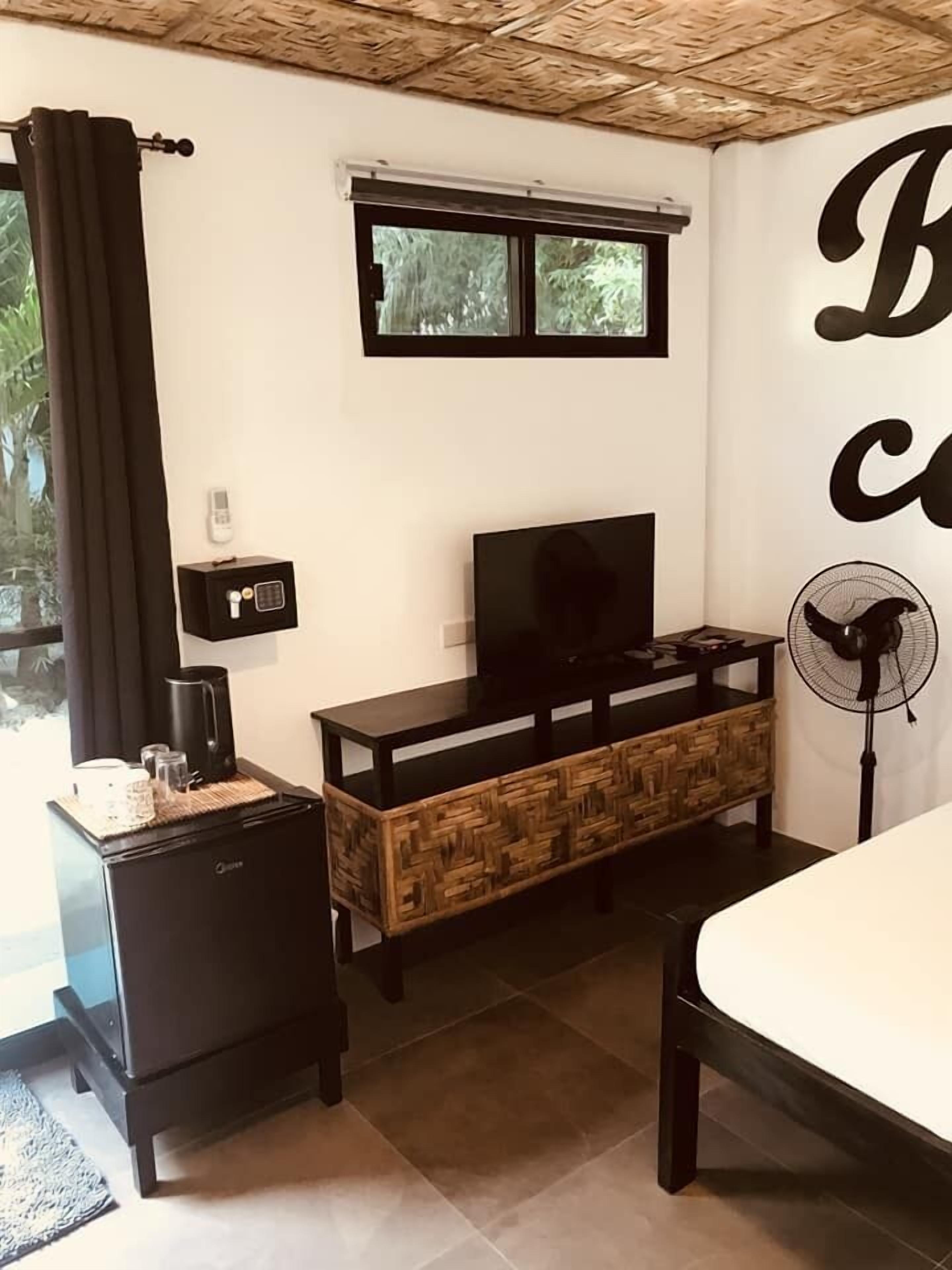 Habitación de hotel compacta con cama, televisor, kitchenette pequeño y ventana con cortinas.