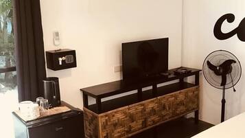 Habitación de hotel compacta con cama, televisor, kitchenette pequeño y ventana con cortinas.