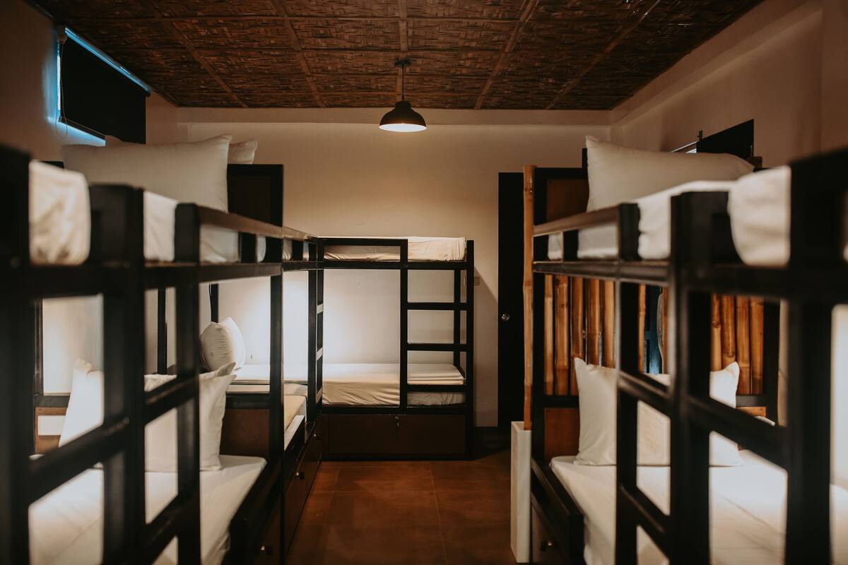 A bunk bed room with a wooden ceiling and a single hanging light fixture.