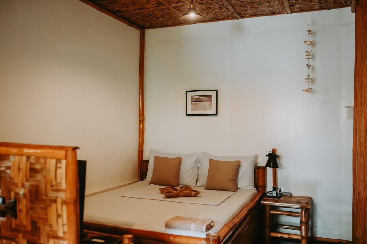 A neatly made bed with pillows and a blanket, a bedside lamp, and a small wooden nightstand.