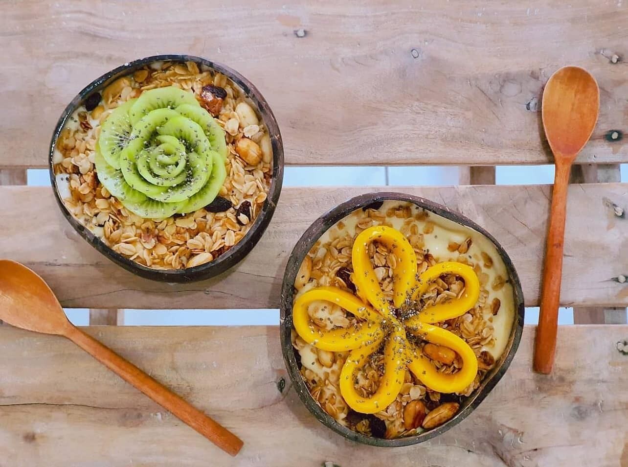 Duas tigelas de cereal sobre uma superfície de madeira, com colheres de pau ao lado.