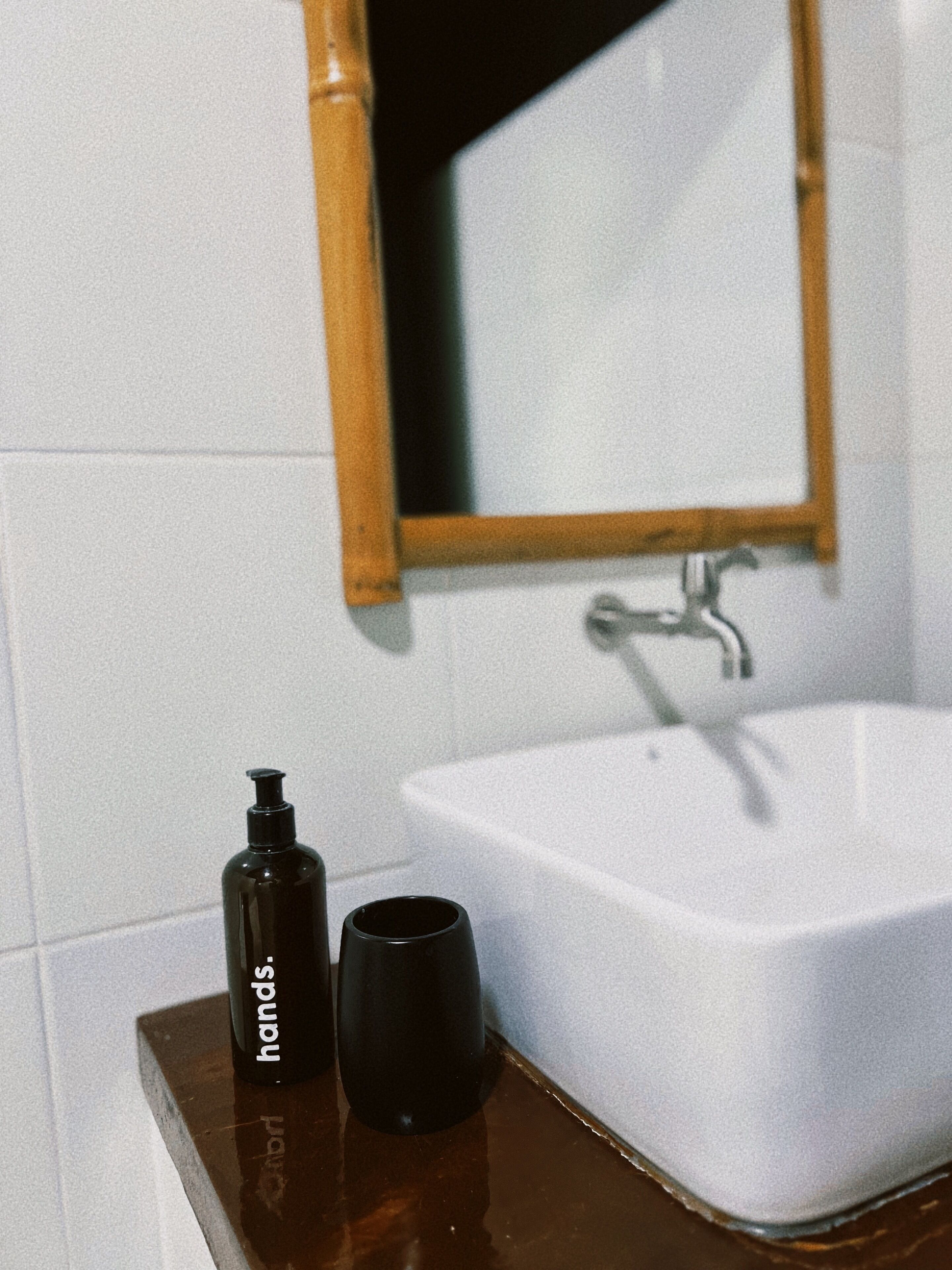 A bathroom with a white sink, a wooden countertop, a black bottle labeled "hands," and a black cup.