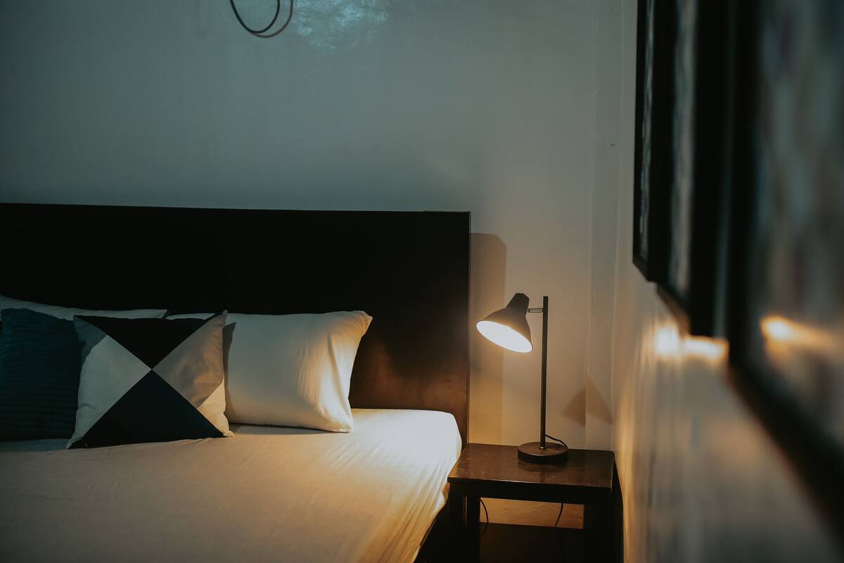 A neatly made bed with a headboard, a bedside lamp, and a wall-mounted clock.