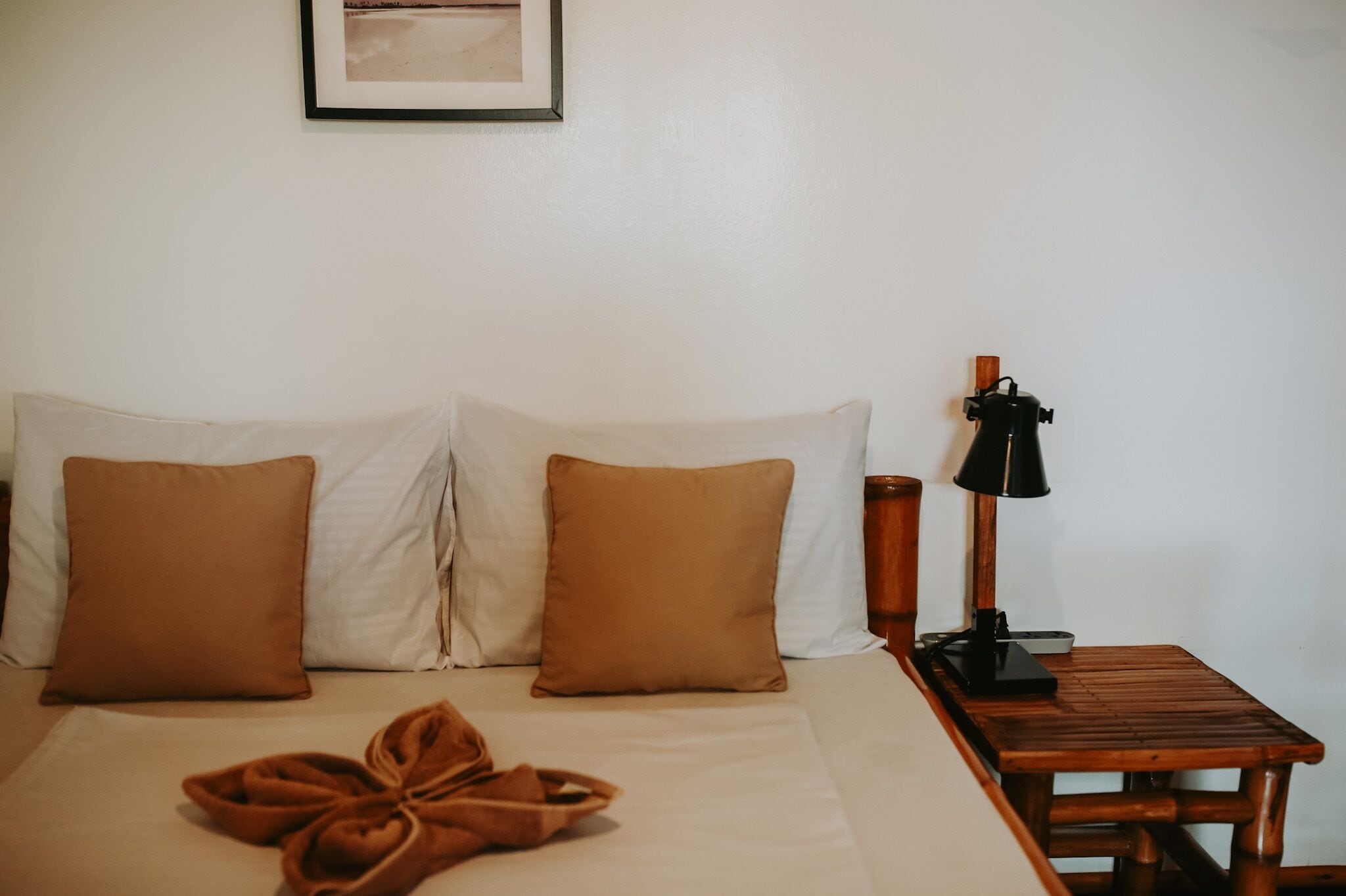Une chambre d’hôtel avec un lit, deux oreillers, une table de chevet avec une lampe et un tableau encadré au mur.