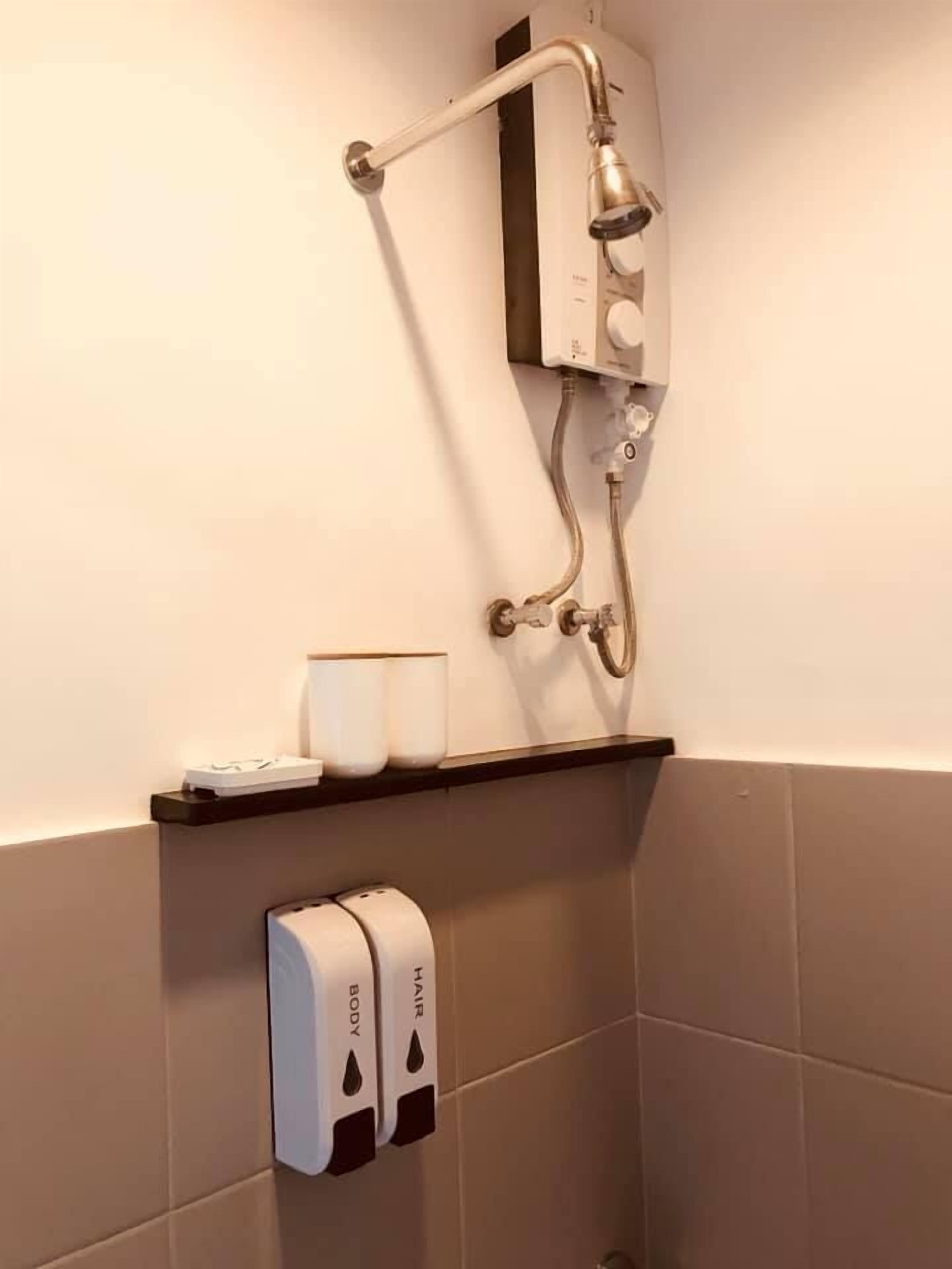 A bathroom with a shower, a towel dispenser, and a soap dispenser on a wall.