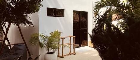 A white building with a small entrance, surrounded by tropical plants and palm trees.