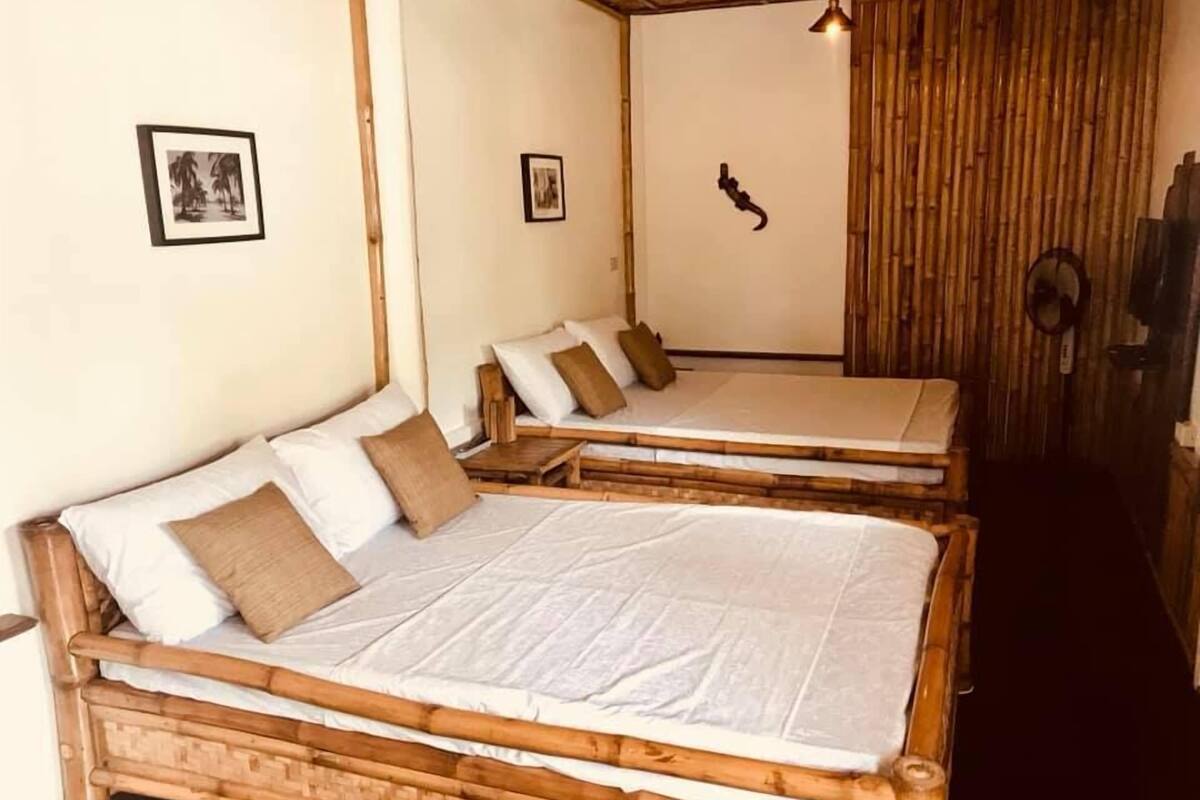 A room with two wooden beds, white bedding, and a bamboo wall.