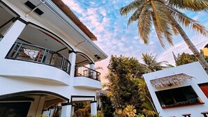 A multi-story building with balconies, surrounded by tropical vegetation.