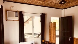 A bedroom with a bed, a nightstand, an air conditioning unit, a window with curtains, and a wooden door.