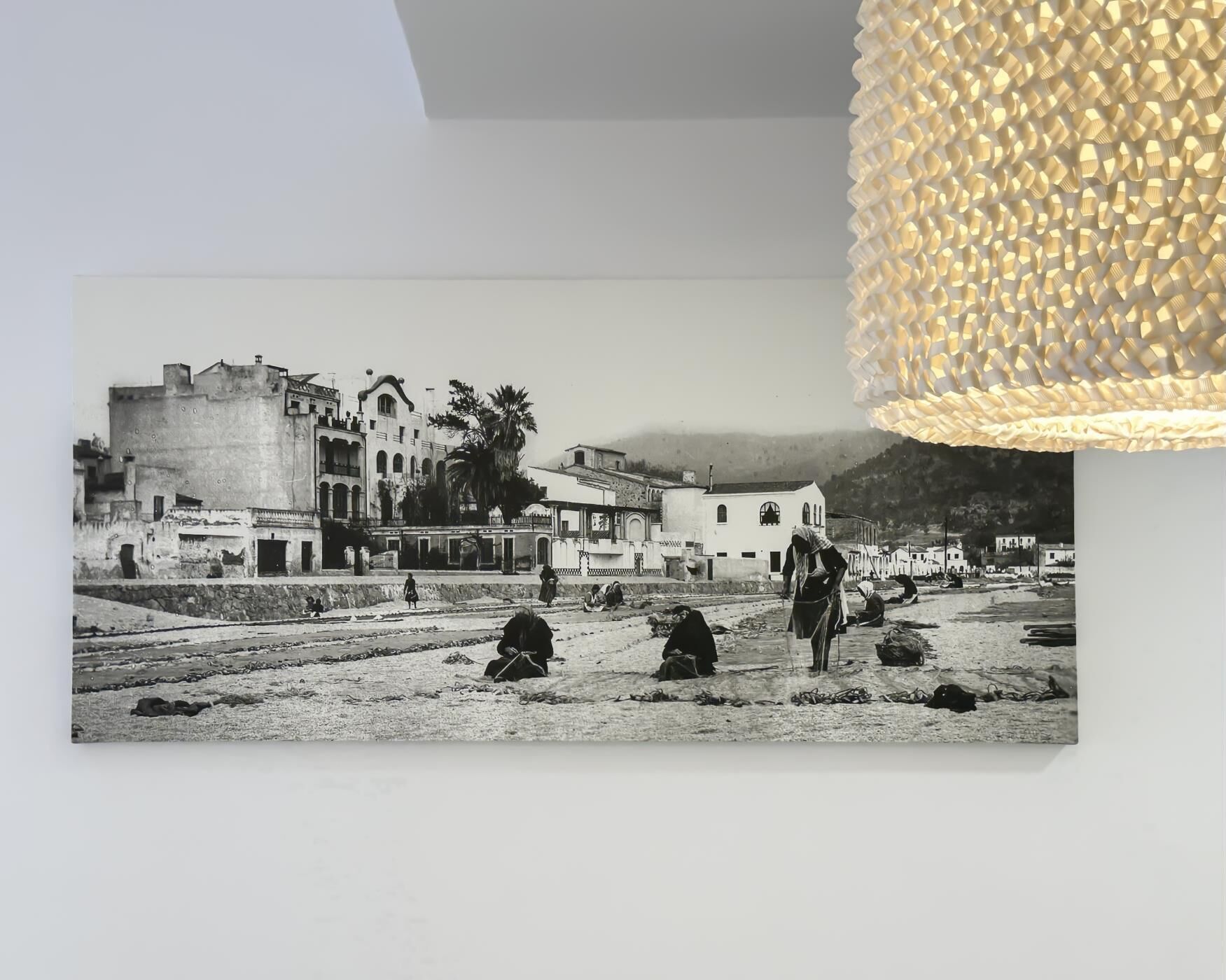 A black and white photograph of a historical building with a balcony, palm trees, and people in traditional attire.