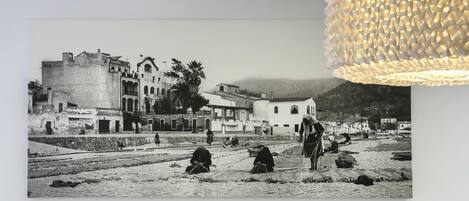 A black and white photograph of a historical building with a balcony, palm trees, and people in traditional attire.