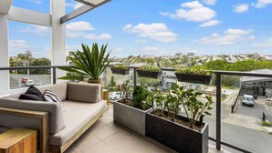 A balcony with a sofa, potted plants, and a view of a cityscape. - Kingsland, Auckland 2BR 2Bath 2CarPark Apt (Auckland)