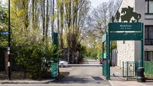 Ein verschlossenes Tor zum Mudchute Park & Farm, mit einem Schild, einem Weg und einem Gebäude im Hintergrund.