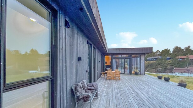 A modern building with a wooden deck, large windows, and outdoor seating. - 3 bedroom lovely home in Lindesnes (Lindesnes)
