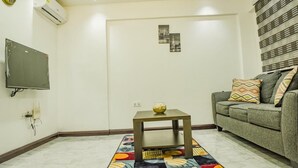 A living room with a sofa, a small table with a bowl, a flat-screen TV, and a patterned rug.