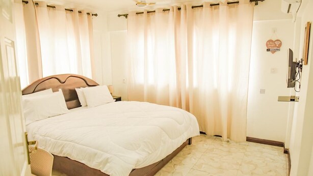 A bedroom with a bed, curtains, a ceiling fan, and a wall-mounted sign.