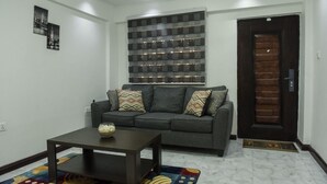A living room with a grey sofa, patterned cushions, a coffee table, and a decorative wall piece.