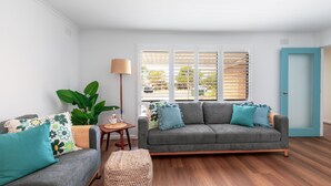 A modern living room with a grey sofa, teal cushions, a floor lamp, a small table with a lamp, and a large plant. - Pet Paradise w/ Fenced yard & close to Beach (Ocean Grove)