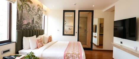 A hotel room with a large bed, a TV, a desk with a phone, a plant, and a mural on the wall.