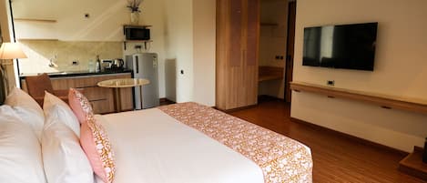 A hotel room with a bed, a TV, a kitchen area, and a dining table.