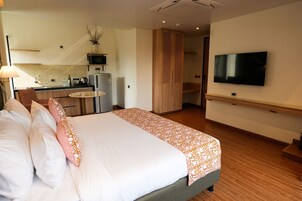 Habitación de hotel con cama, televisión, kitchenette y mesa de comedor.
