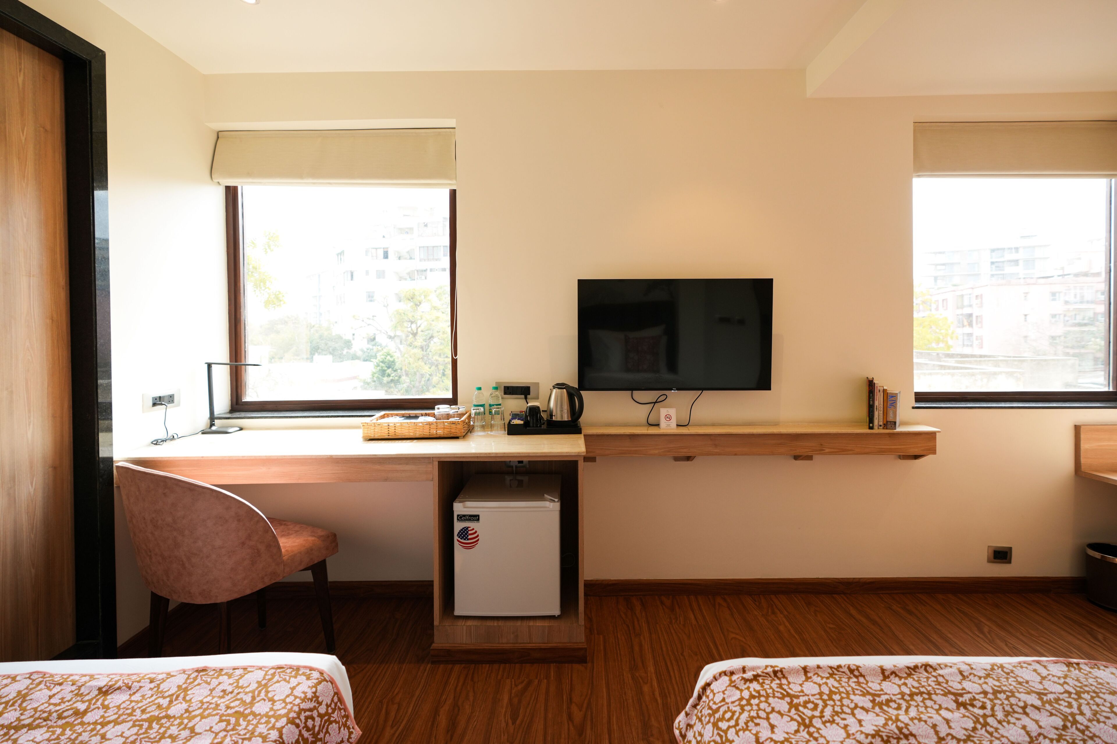 A hotel room with a bed, a desk with a computer, a television, and a small refrigerator.