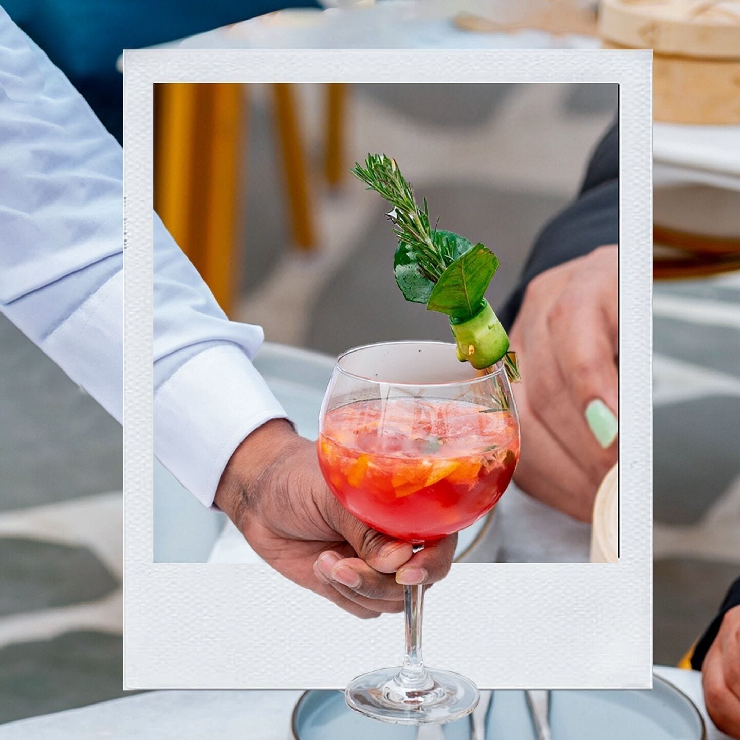 A person holding a glass with a garnish, possibly containing a cocktail.