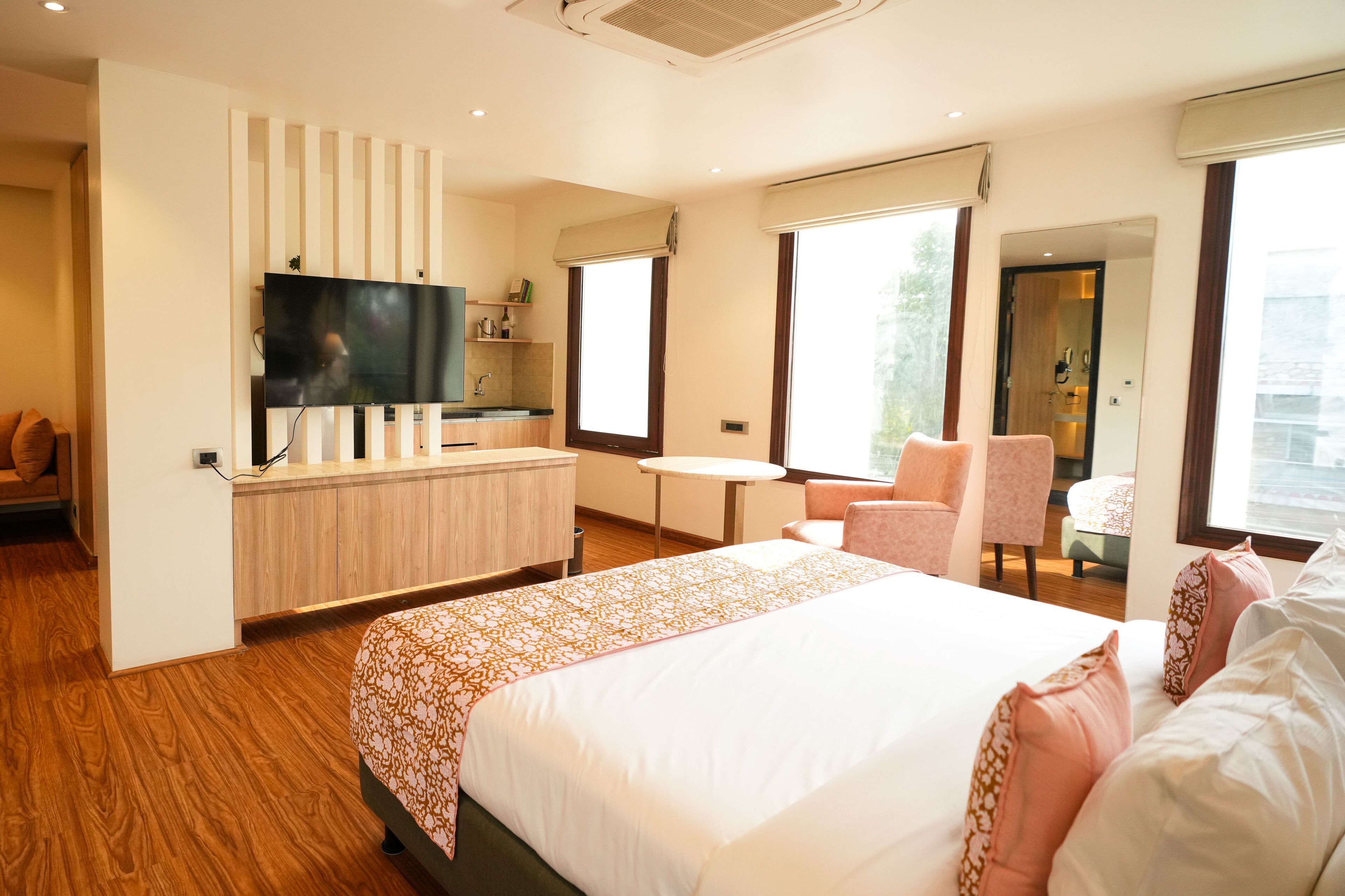 Ein modernes Hotelzimmer mit einem großen Bett, einem an einer Holzplatte montierten Fernseher, einem kleinen Tisch, einem Sessel und einem Fenster mit Blick.