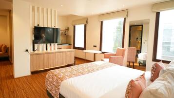 Habitación de hotel moderna con una cama grande, un televisor montado en un panel de madera, una mesita, una silla y una ventana con vistas.