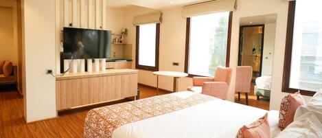 Habitación de hotel moderna con una cama grande, un televisor montado en un panel de madera, una mesita, una silla y una ventana con vistas.