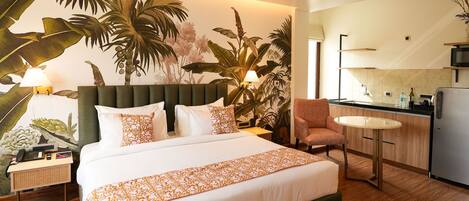 A hotel room with a large bed, a small round table, a kitchenette, and a view of the outside.