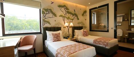 A hotel room with two beds, a desk, and a chair. There is a large window, a mirror, and a wall with a tree mural.