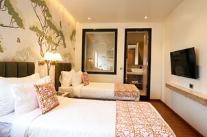 Quarto de hotel com duas camas, uma televisão, um espelho e um banheiro visível através de uma porta de vidro.