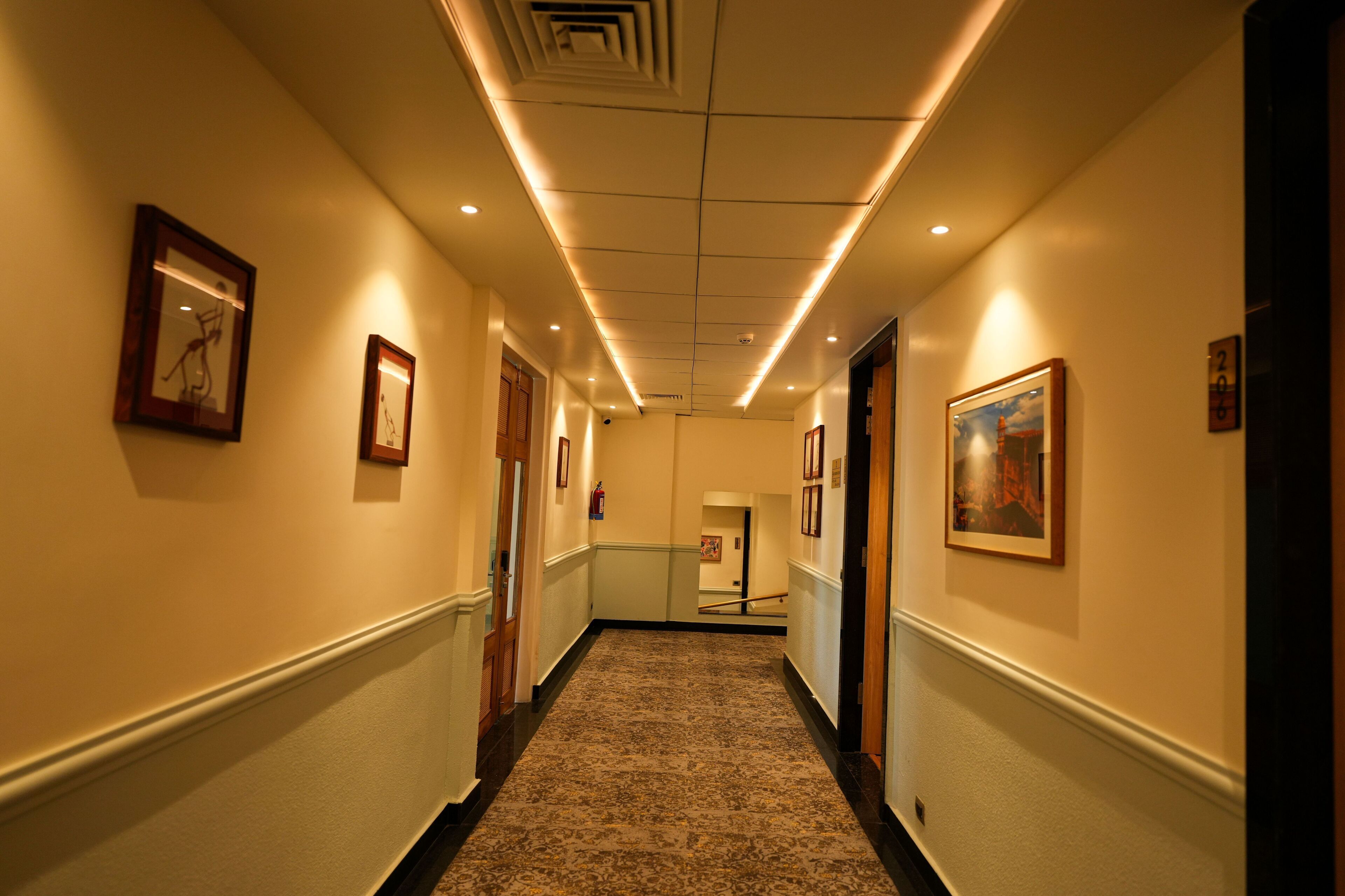 A hotel hallway with framed artwork on the walls, a carpeted floor, and a ceiling with recessed lighting.