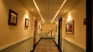 A hotel hallway with framed artwork on the walls, a carpeted floor, and a ceiling with recessed lighting.