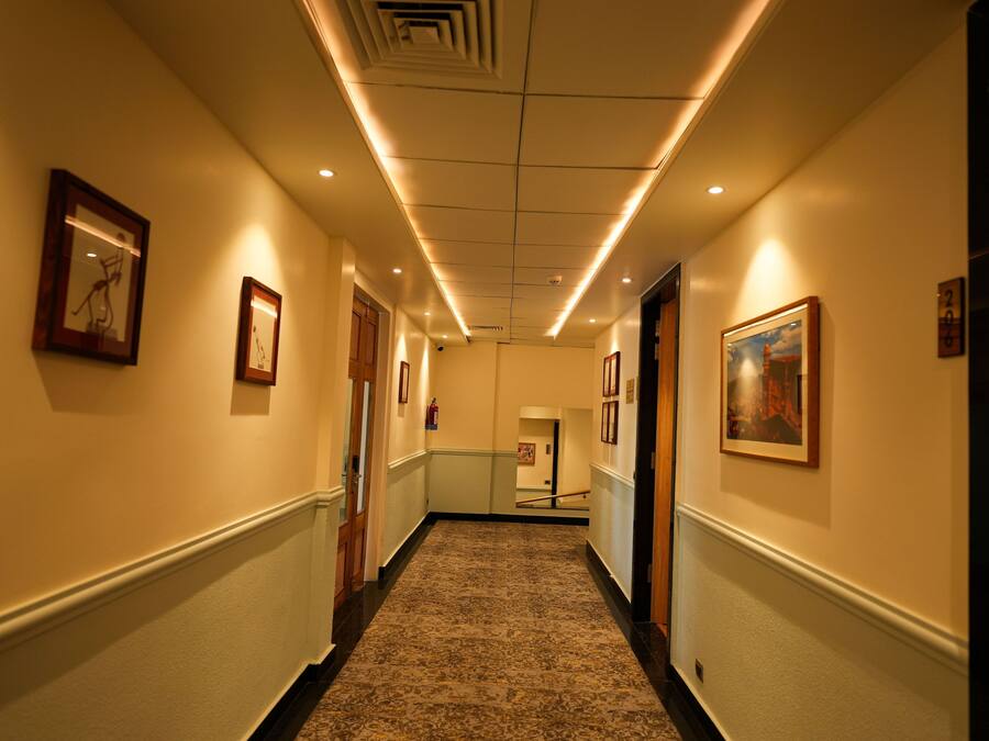 Un couloir d’hôtel avec des œuvres d’art encadrées accrochées aux murs, un sol recouvert de moquette et un plafond doté d’un éclairage encastré.