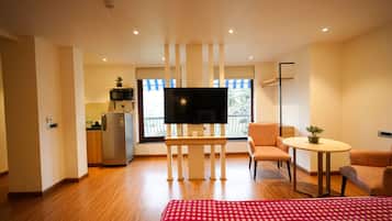 Habitación de hotel con cama, televisión, mesita, silla, kitchenette y balcón con vistas.