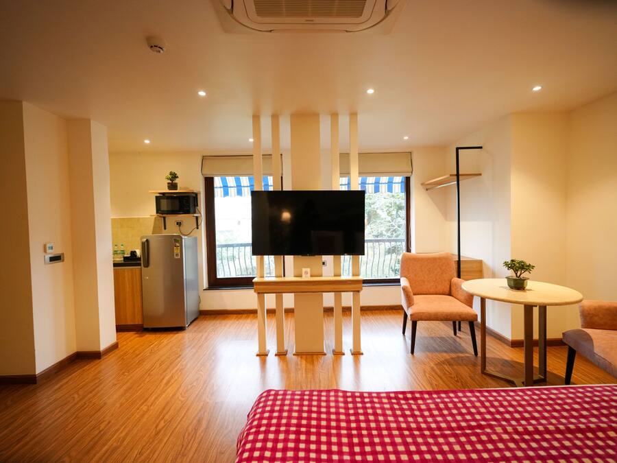 Habitación de hotel con cama, televisión, mesita, silla, kitchenette y balcón con vistas.