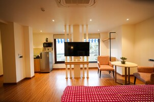 Quarto de hotel com cama, televisão, mesinha, cadeira, cozinha compacta e varanda com vista.