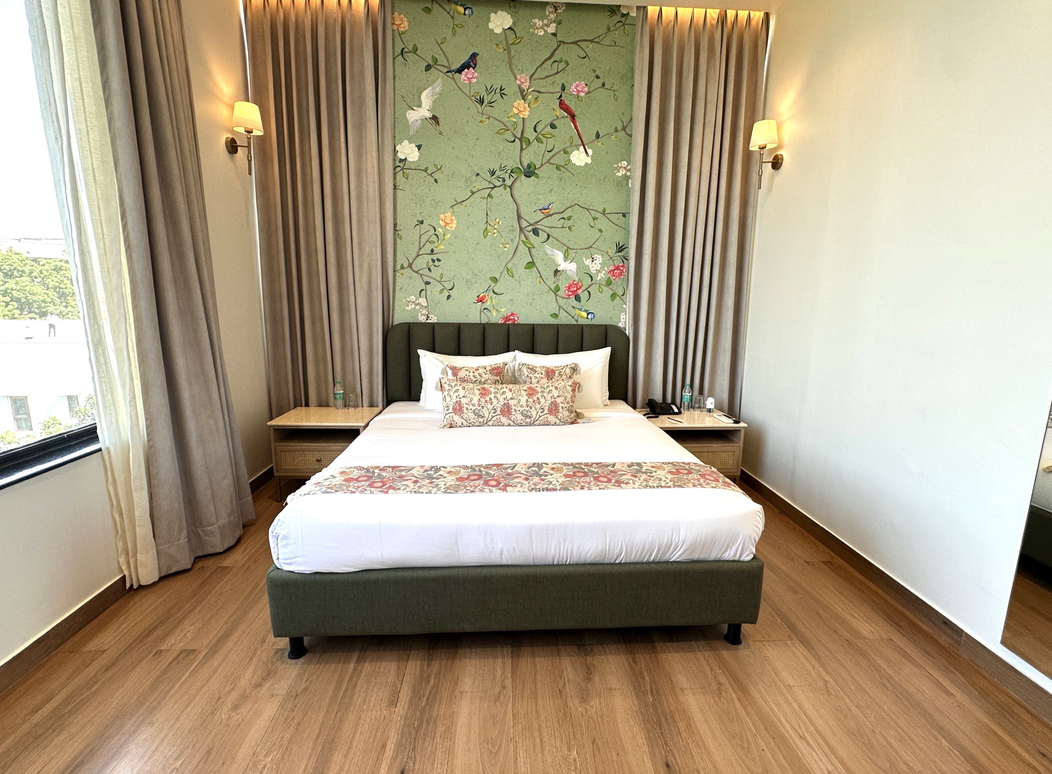 Een hotelkamer met een groot bed, nachtkastje, lamp en een bloemendecoratie op de muur.