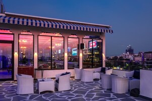 Terraço no telhado com área de estar externa e grandes janelas com vista para a cidade.