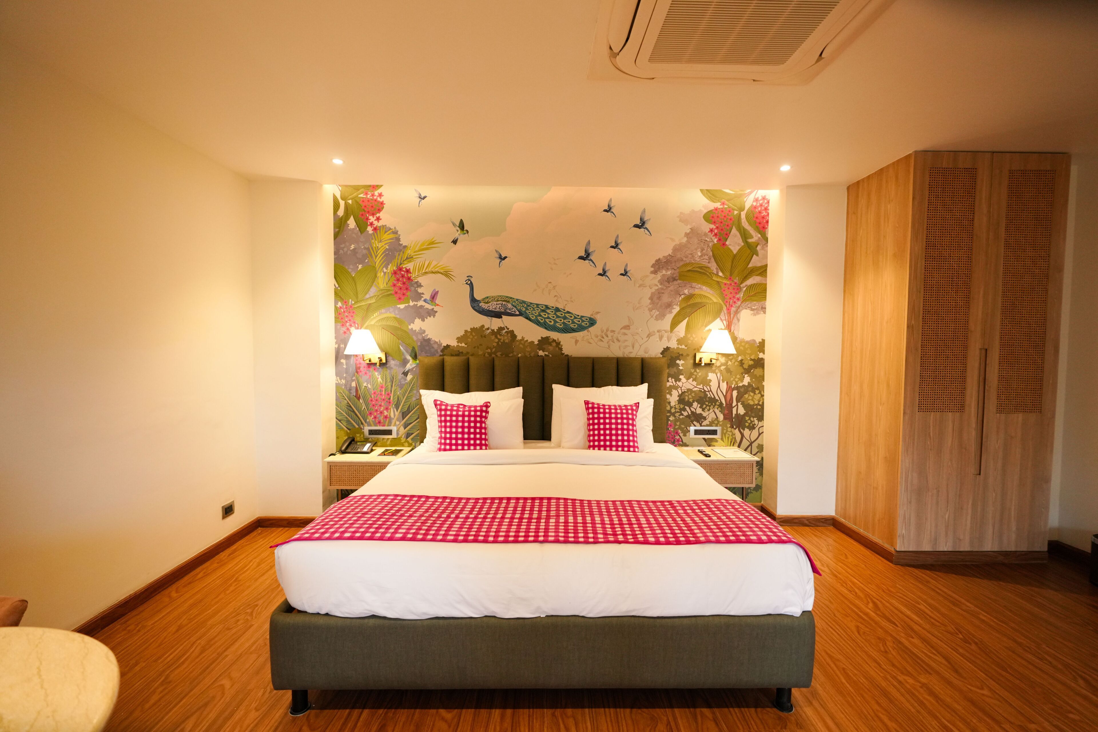 A hotel room with a large bed, a wooden wardrobe, and a mural with birds and peacocks on the wall.