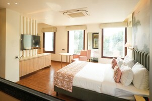 Quarto de hotel com uma cama grande, uma escrivaninha, uma cadeira e uma televisão.