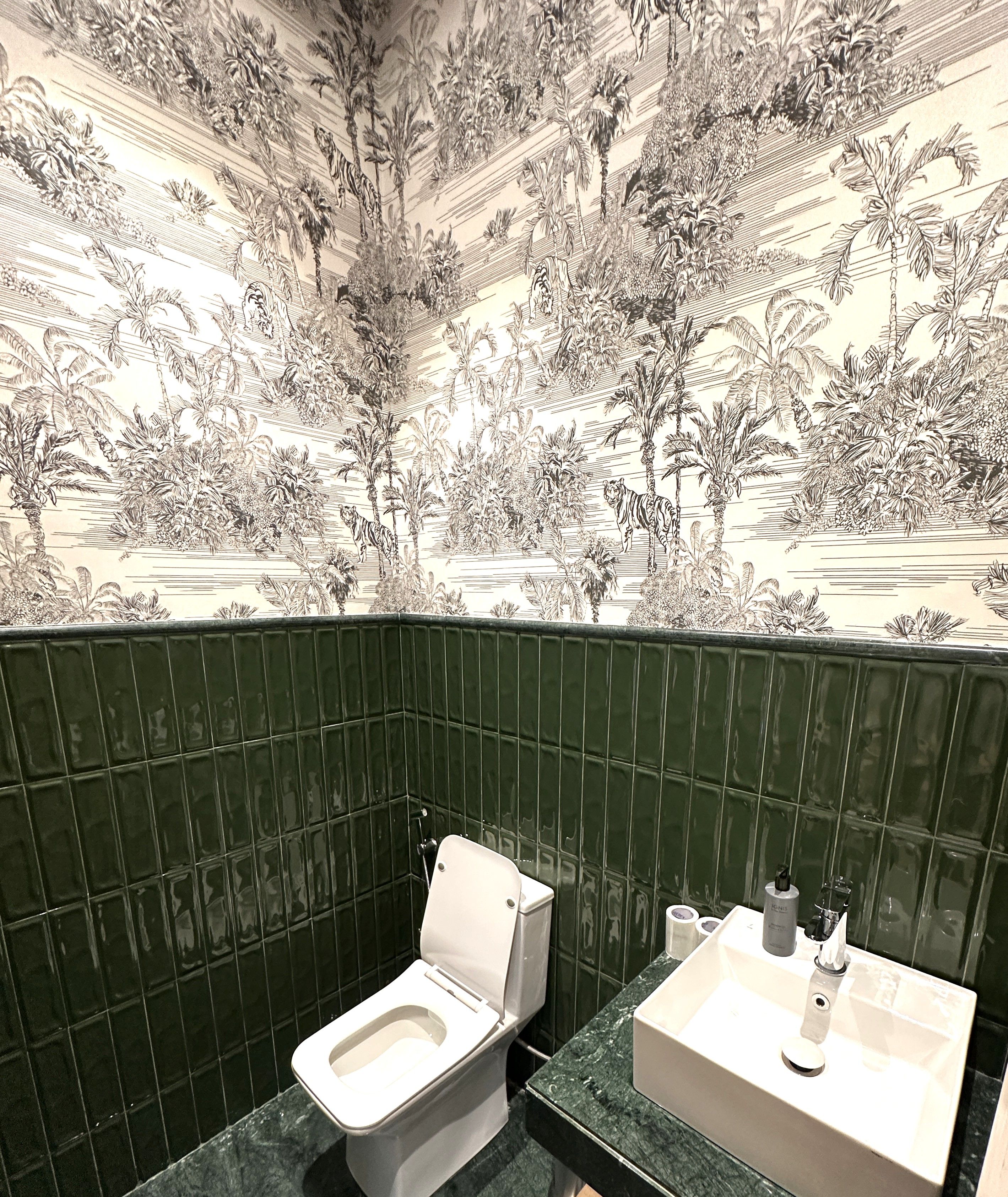 Un baño con inodoro, lavabo y paredes con azulejos verdes.