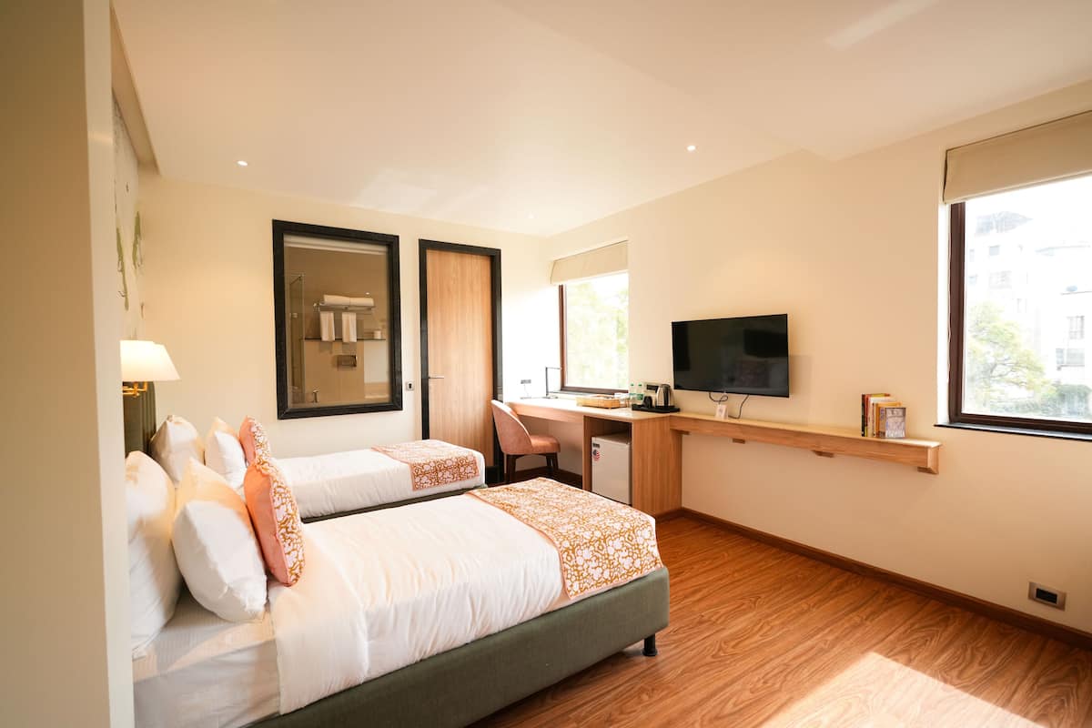 Habitación de hotel con dos camas, un escritorio, televisor y ventana.