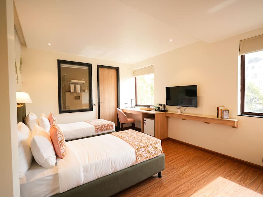Habitación de hotel con dos camas, un escritorio, televisor y ventana.