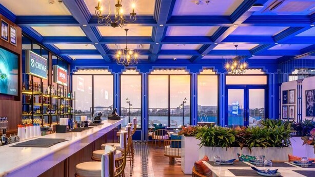 A bar area with a view of the city skyline, featuring a bar counter, seating, and large windows.